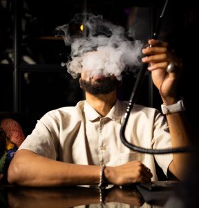 Man smoking hookah with smoke in dark room